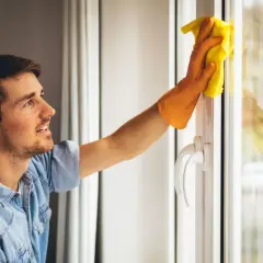Un homme souriant nettoie une fenêtre en aluminium blanc avec un chiffon jaune.