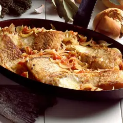 Morue à la lyonnaise, des filets de poisson dorés mijotant avec des oignons et des tomates dans une poêle.