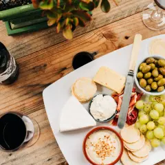 Un plateau de fromages variés, charcuterie, olives et raisins, accompagné d'une bouteille et d'un verre de vin rouge. Quel vin rouge avec un plateau de fromage varié ?