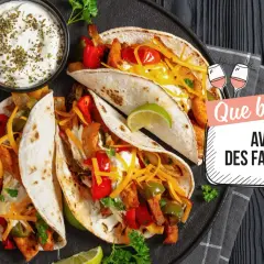 Assiette de fajitas savoureuses avec garnitures, crème aigre et quartiers de citron vert. Le texte demande "Que boire avec des fajitas ?".