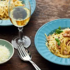 Un délicieux vin blanc accompagne un plat de spaghetti carbonara, garni de parmesan râpé et de basilic frais.