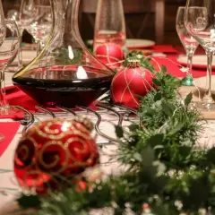 Table dressée pour Noël avec carafe de vin rouge. Combien de cubi de vin pour 40 personnes ? Boules rouges et guirlande verte.