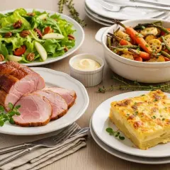 Un rôti de porc froid tranché, servi avec une salade verte croquante, des légumes rôtis et un gratin dauphinois. Parfait pour accompagner un rôti de porc froid.