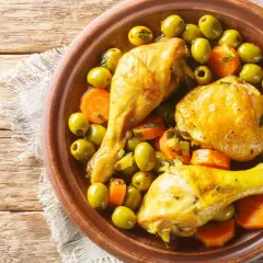 Un plat de tajine poulet citron avec des olives vertes et des carottes, servi dans un plat en terre cuite sur une table en bois.