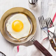 Un œuf au plat parfait, cuisiné dans une poêle inox, prêt à être dégusté avec deux fourchettes.
