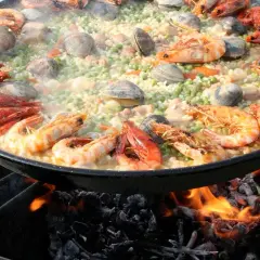 Gros plan sur une paella aux crevettes et palourdes, cuisant sur un feu de bois. Quel vin avec jambalaya ? Un blanc sec ou un rosé fruité serait parfait.