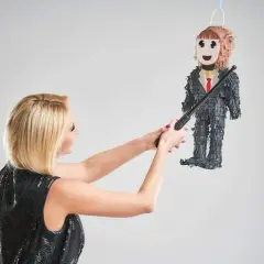 Une femme en robe à paillettes s'apprête à frapper une piñata en forme d'homme en costume, symbole d'une fête de divorce réussie.