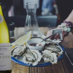 Une bouteille de Chablis Grand Cru William Fèvre, parfaite pour savoir quoi boire avec des huîtres. Une assiette d'huîtres fraîches et un quartier de citron complètent la scène.