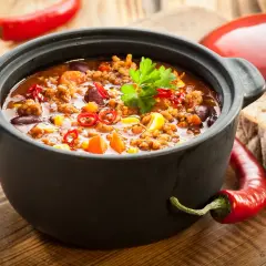 Un plat de chili mijoté dans une cocotte en fonte, parfait pour savoir si l'on peut mettre une cocotte en fonte au four. Accompagné de pain et de piments.