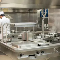 Un chef travaille dans une cuisine professionnelle étincelante, tout en acier inoxydable, le meilleur inox pour une hygiène parfaite.