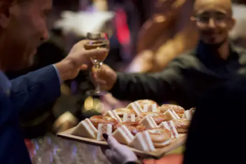 Deux hommes portent des verres et un plateau de mini-sandwichs et de bagels, prêts pour une boisson soirée.