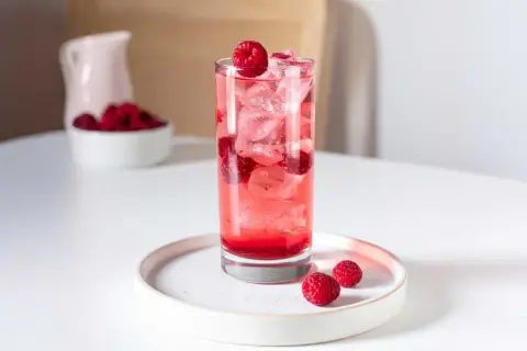 Verre de boisson sans alcool aux framboises, parfait pour accompagner un repas. Glaçons et fruits frais pour une touche rafraîchissante.