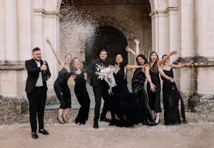 Un groupe joyeux célèbre un mariage noir et blanc, le marié aspergeant de champagne ses demoiselles d'honneur en robe noire.