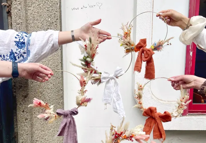 Des mains créatives assemblent des couronnes de fleurs séchées lors d'un atelier EVJF. Ambiance bohème et festive.