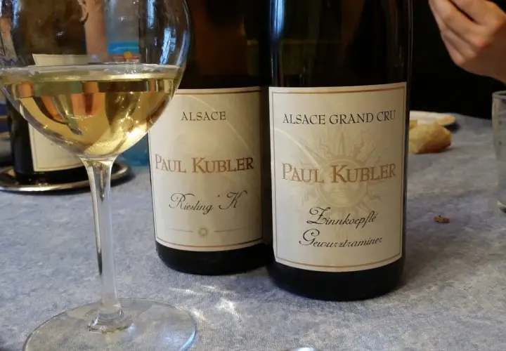 Verre de vin blanc alsacien, idéal pour accompagner une choucroute. Deux bouteilles Paul Kubler Riesling K et Gewurztraminer sont visibles.