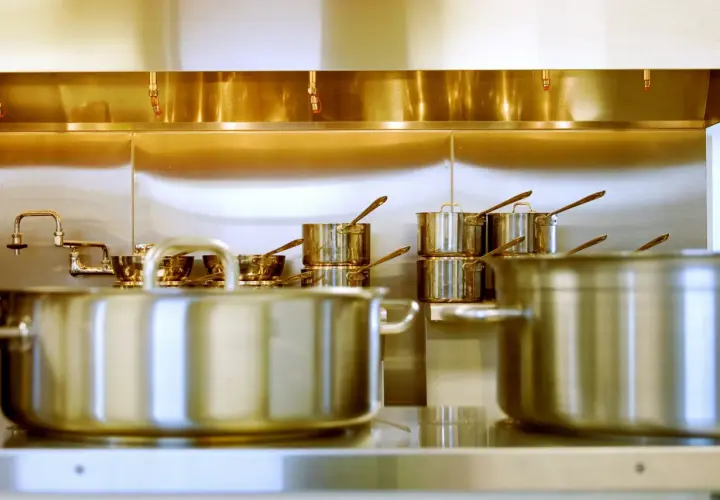 Une cuisine professionnelle avec des casseroles en inox 18/0 étincelantes sous une hotte aspirante.