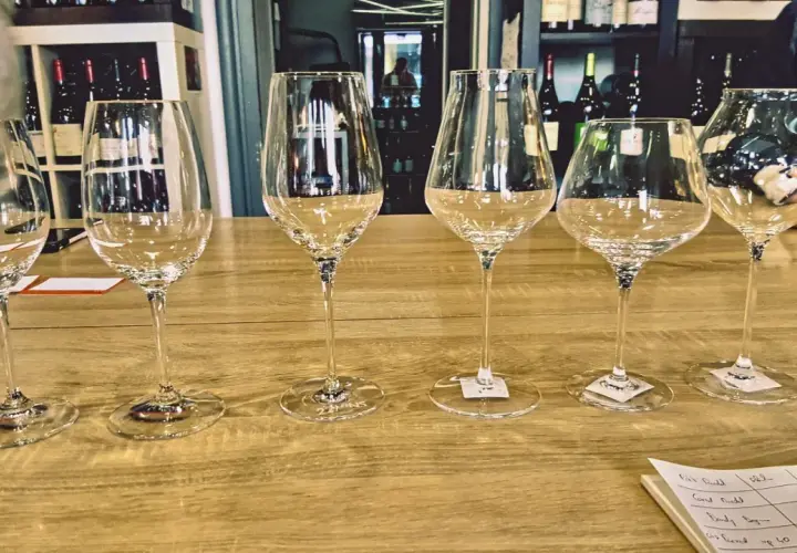 Six verres à vin vides alignés sur un comptoir de bar en bois, prêts pour une dégustation.