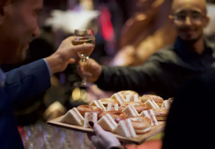Deux hommes portent des verres et un plateau de mini-sandwichs et de bagels, prêts pour une boisson soirée.