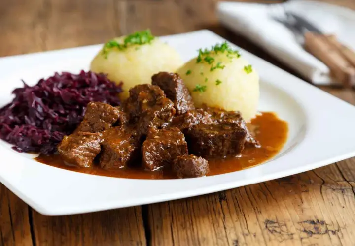 Un plat appétissant de daube de sanglier au vin blanc, servi avec des quenelles et du chou rouge.