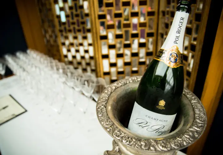 Bouteille de champagne Pol Roger dans un seau à glace, avec des flûtes alignées en arrière-plan.
