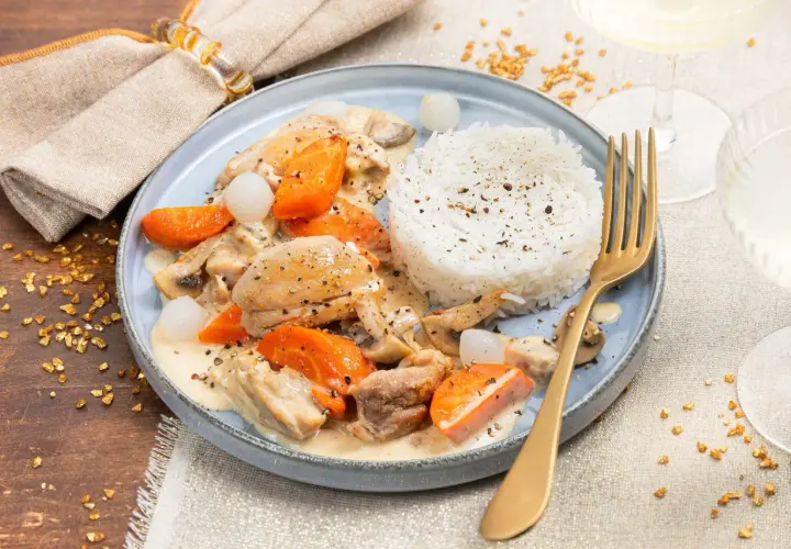 Un plat de dinde à la crème avec carottes, champignons et riz blanc. Un verre de vin blanc à côté.