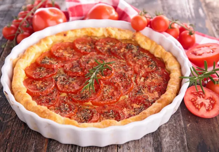 Tarte aux tomates fraîches, garnie d'herbes et d'une branche de romarin. Un accompagnement tarte tomate parfait pour un repas d'été.