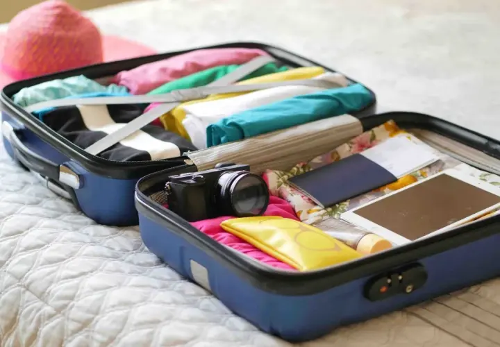 Valise ouverte prête pour un EVJF : vêtements colorés, appareil photo, passeport, tablette. Une liste valise EVJF drôle à compléter !