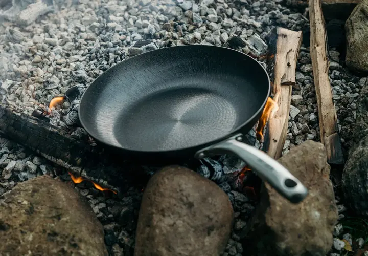 Poêle posée sur des braises et des pierres, prête à redresser le fond d'une poêle pour une cuisson en plein air.
