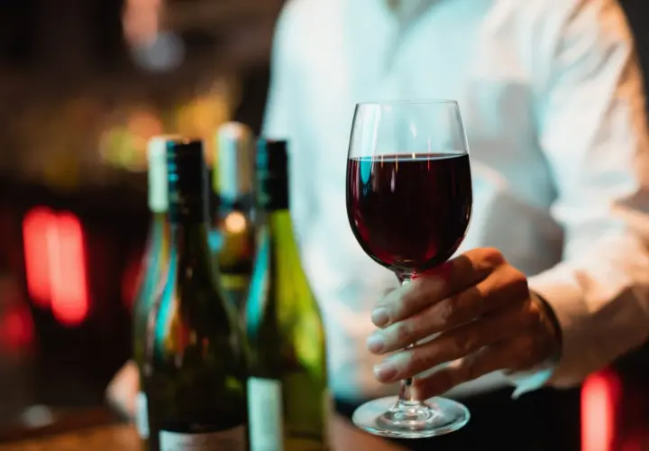 Main tenant d'un verre de bon beaujolais, avec des bouteilles en arrière-plan.