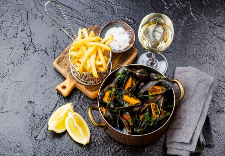 Un plat de moules frites, accompagné de quartiers de citron, d'une coupelle de gros sel et d'un verre de vin blanc.