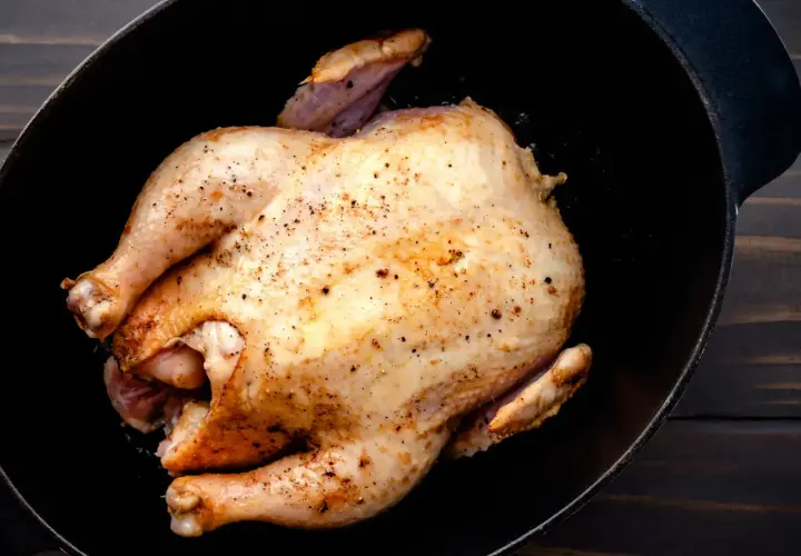 Un poulet rôti doré, assaisonné de poivre, repose dans une cocotte en fonte. Un délice prêt à être dégusté, un vrai poulet Calvi.
