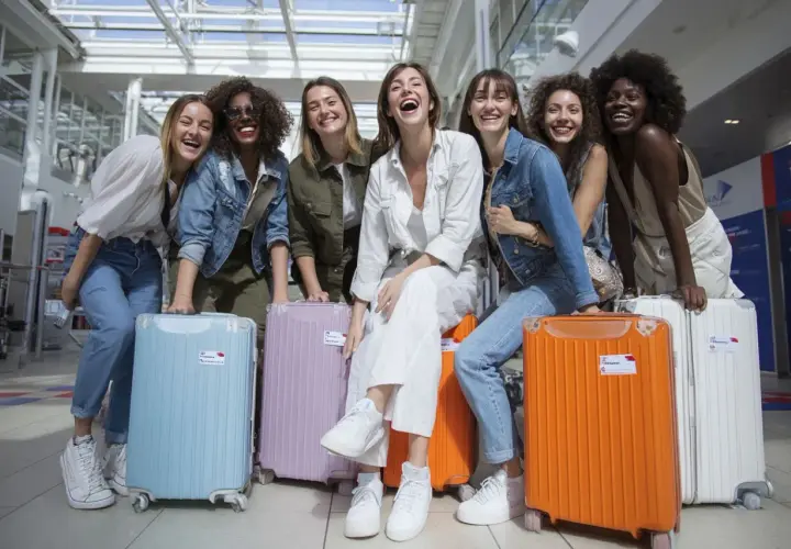 Groupe de femmes joyeuses à l'aéroport avec leurs valises colorées, prêtes pour une destination EVJF pas cher.