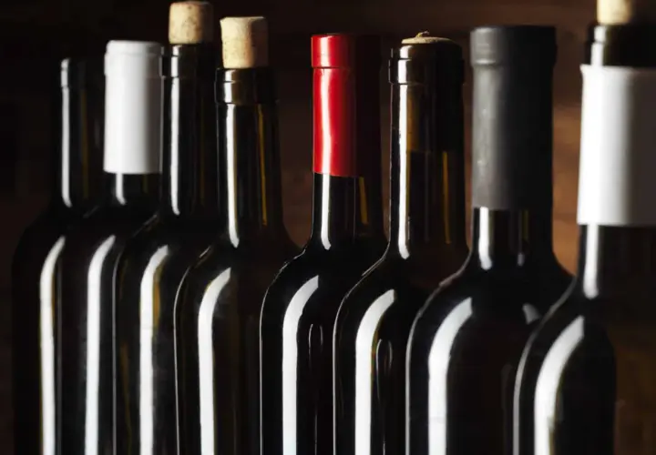 Une rangée de bouteilles de vin sombres, certaines avec des bouchons en liège, d'autres avec des capsules colorées. Un millésime Beaujolais pourrait se cacher parmi elles.