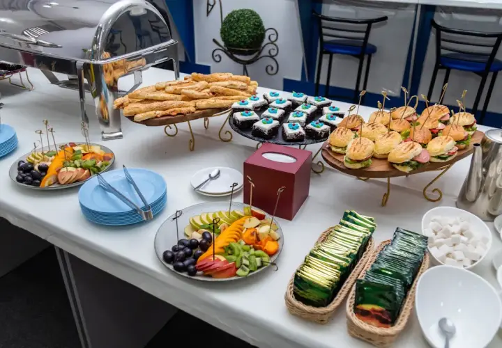 Un buffet de hors d'œuvre varié avec mini-burgers, pâtisseries, bâtonnets feuilletés et salade de fruits.