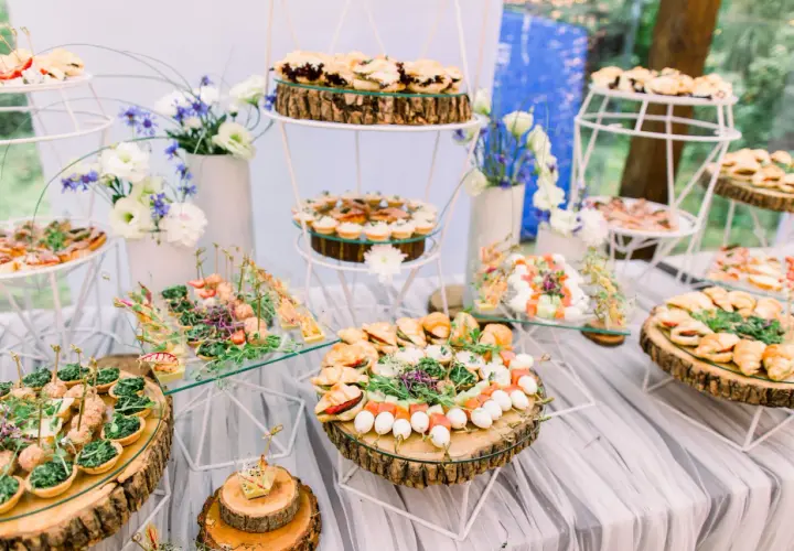 Un buffet de mariage participatif avec une variété de petits fours, tartines et brochettes, joliment présentés sur des rondins de bois et des étagères en verre.