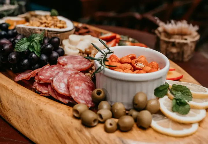 Un buffet campagnard pour 20 personnes : raisins noirs, salami, olives, cacahuètes épicées, citron et menthe sur un plateau en bois.