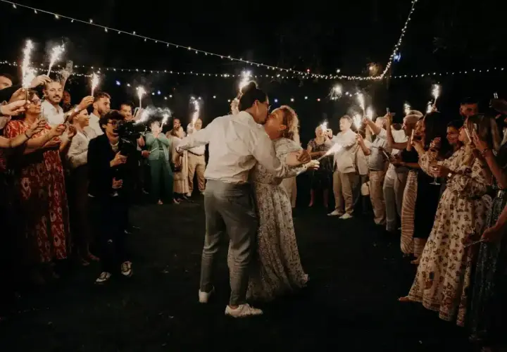 Mariage intime pour 30 personnes : le couple s'embrasse sous les feux de la rampe, entouré de ses proches.