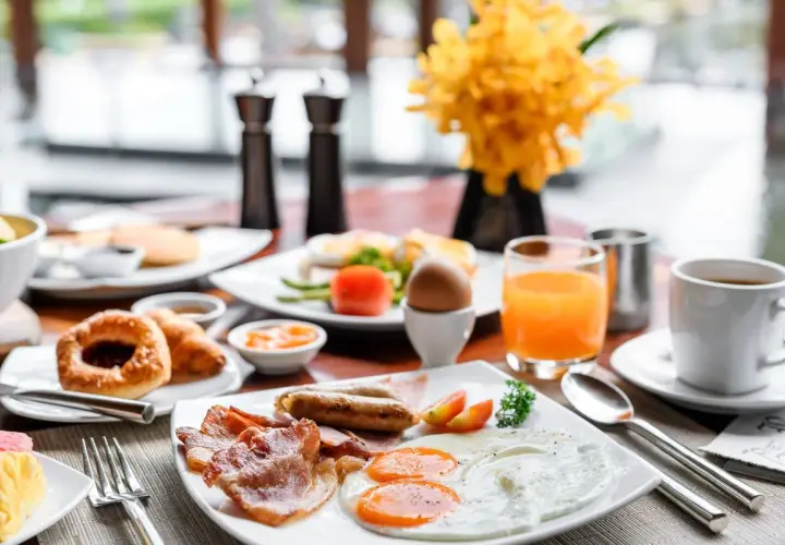 Un copieux petit déjeuner continental ou américain avec œufs, bacon, saucisses, viennoiseries, jus d'orange et café.