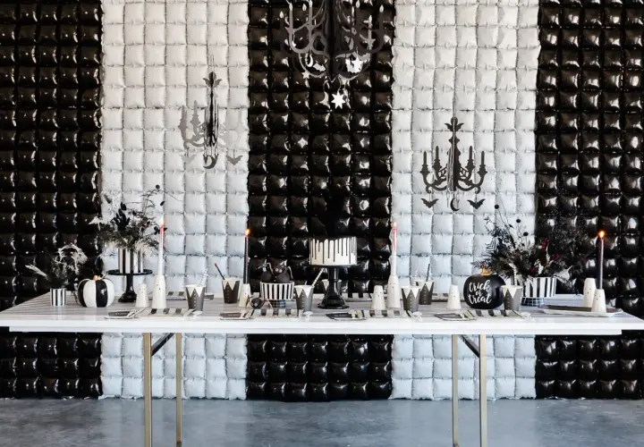 Table dressée pour une activité anniversaire mercredi Addams : gâteau, citrouille, décorations gothiques sur fond rayé noir et blanc.