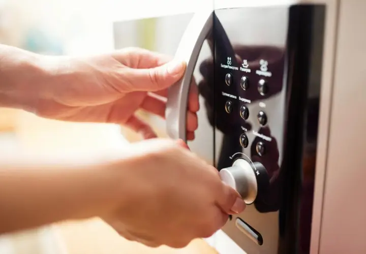 Mains de femme ouvrant un micro-ondes en inox. Elle tourne le bouton pour régler le temps de cuisson.