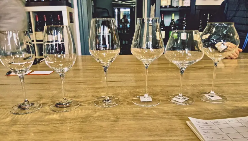 Six verres à vin vides alignés sur un comptoir de bar en bois, prêts pour une dégustation.