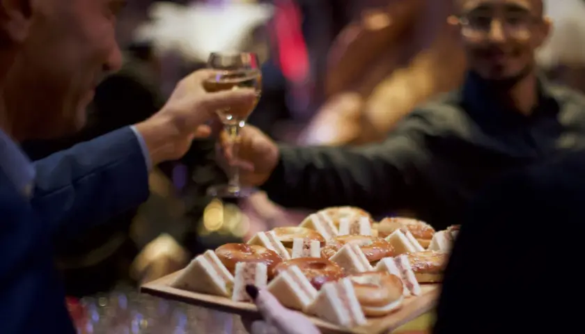 Deux hommes portent des verres et un plateau de mini-sandwichs et de bagels, prêts pour une boisson soirée.