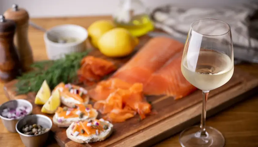 Un verre de vin blanc, parfait pour accompagner le saumon fumé, est présenté avec des toasts, des câpres, des oignons rouges et du citron.