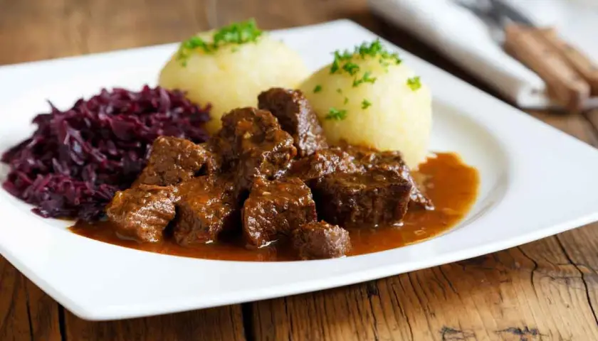 Un plat appétissant de daube de sanglier au vin blanc, servi avec des quenelles et du chou rouge.
