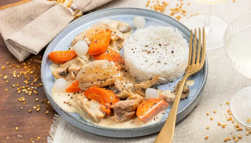 Un plat de dinde à la crème avec carottes, champignons et riz blanc. Un verre de vin blanc à côté.