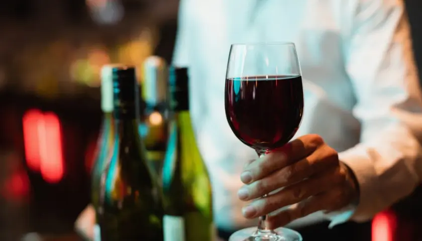Main tenant d'un verre de bon beaujolais, avec des bouteilles en arrière-plan.