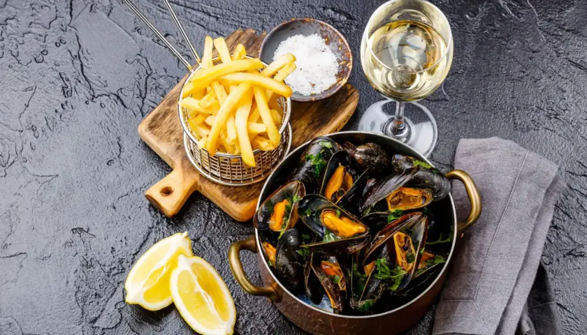 Un plat de moules frites, accompagné de quartiers de citron, d'une coupelle de gros sel et d'un verre de vin blanc.