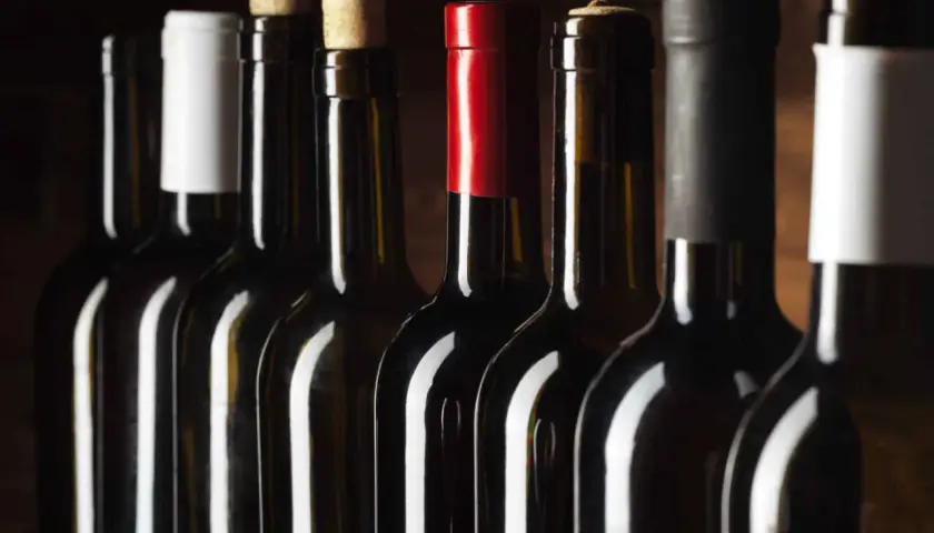 Une rangée de bouteilles de vin sombres, certaines avec des bouchons en liège, d'autres avec des capsules colorées. Un millésime Beaujolais pourrait se cacher parmi elles.