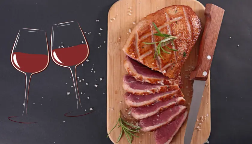 Un plat de magret de canard tranché, garni de romarin, prêt à être dégusté avec deux verres de vin rouge.