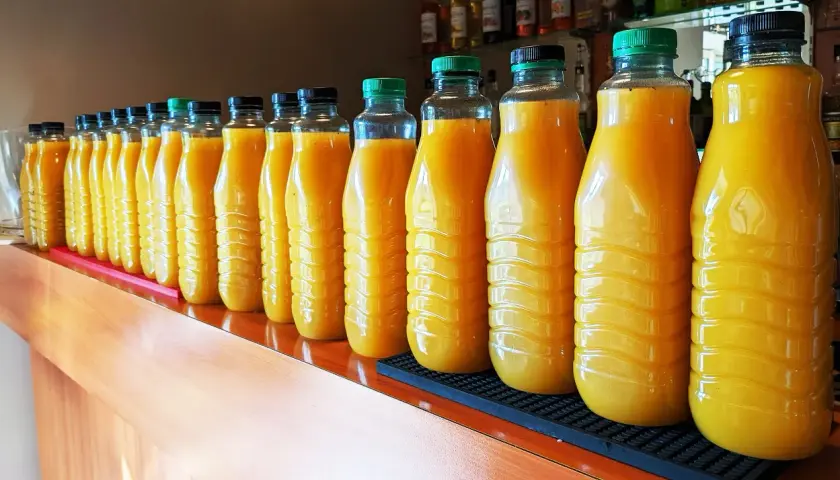 Une longue rangée de bouteilles de jus d'orange, prêtes pour une fête. 5 litres de punch pour combien de personnes ?